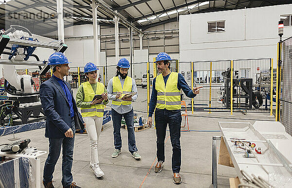 Ingenieure mit Schutzhelmen diskutieren in einer Roboterfabrik