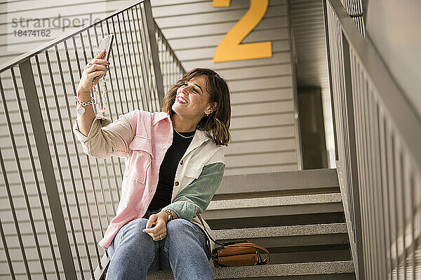 Glückliche Frau  die auf der Treppe sitzt und ein Selfie mit ihrem Smartphone macht