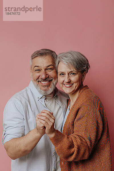 Lächelndes reifes Paar  das zusammen vor rosa Hintergrund steht