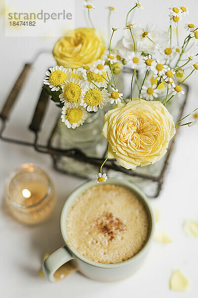 Tasse Kaffee mit gelben und weißen Blumen auf dem Tisch