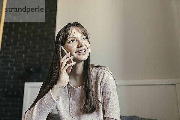 Lächelnde junge Frau  die zu Hause im Schlafzimmer mit dem Smartphone spricht
