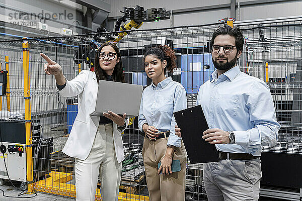 Geschäftsfrau mit Laptop zeigt Kollegen in der Fabrik