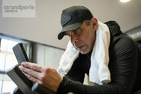 Konzentrierter Mann mit Mütze und Smartphone im Fitnessstudio