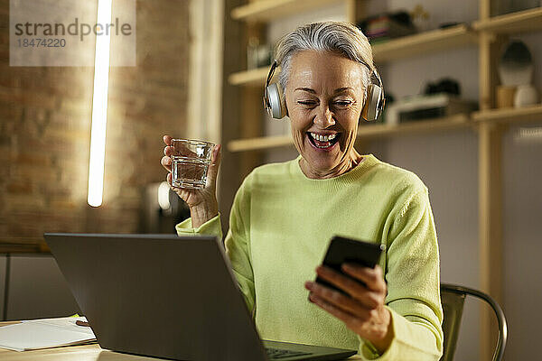 Glückliche Frau mit einem Glas Wasser und einem Smartphone zu Hause