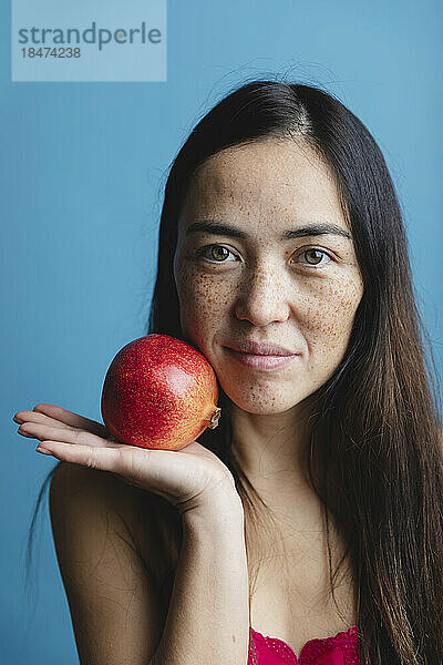 Lächelnde Frau hält Granatapfelfrüchte vor blauem Hintergrund