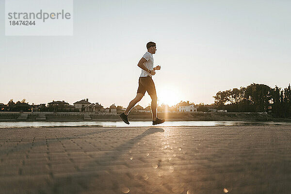 Junger Mann läuft bei Sonnenuntergang auf Fußweg