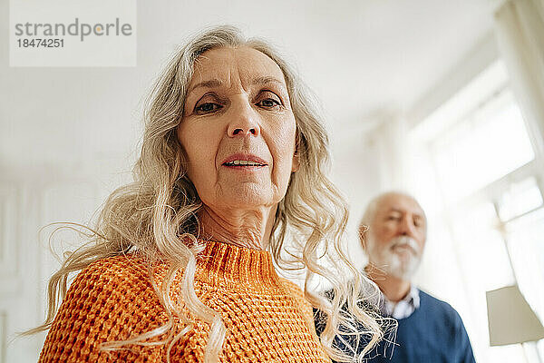 Ältere Frau mit Mann im Hintergrund zu Hause