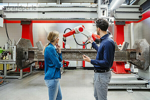 Ingenieur erklärt Kollegen  die in der Fabrik stehen  Roboter