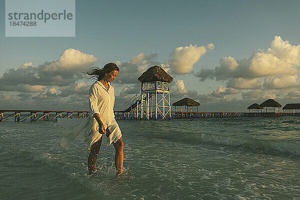 Junge Frau spaziert im Morgengrauen im Meer am Strand