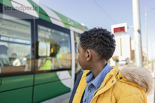 Junge im Parka-Mantel schaut auf die Straßenbahn