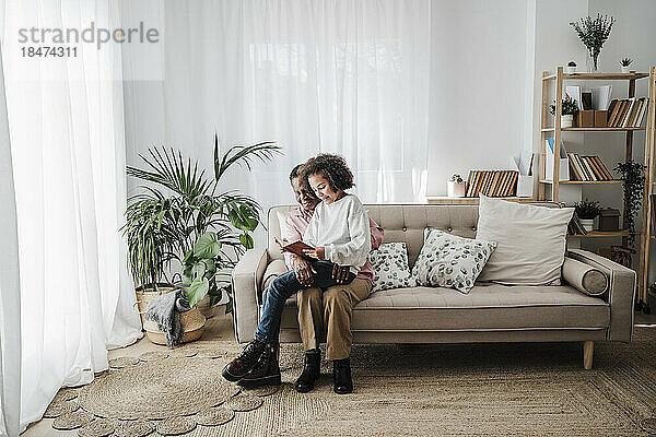Mädchen teilt Buch mit Großmutter  die zu Hause auf dem Sofa sitzt