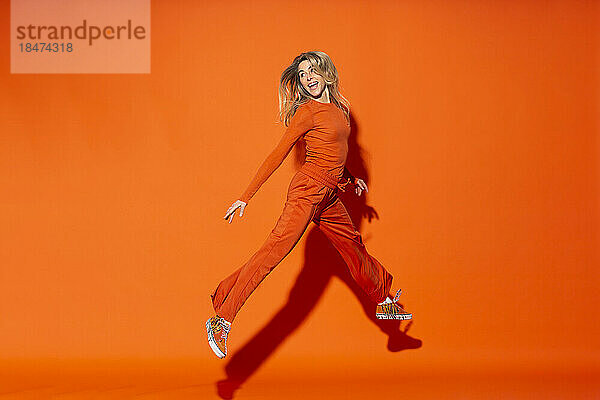 Sorglose Frau springt vor orangefarbenem Hintergrund