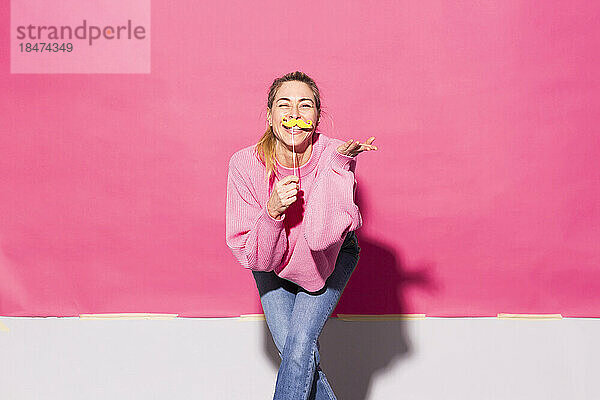 Frau hat Spaß mit falschem Schnurrbart vor rosa Hintergrund