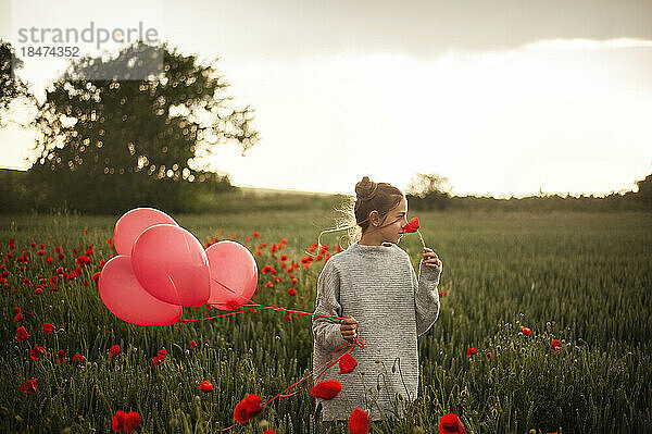 Mädchen hält Luftballons und duftet nach Mohnblume