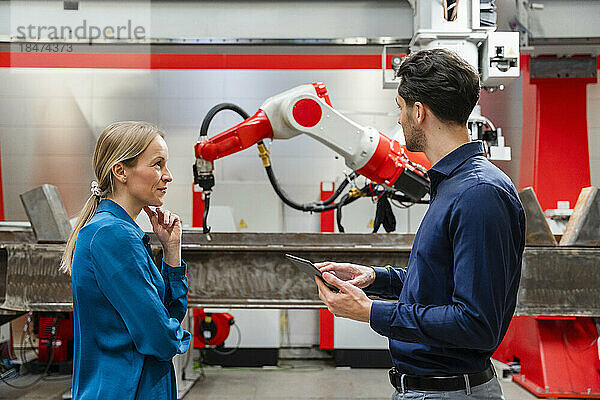 Reifer Ingenieur schaut Techniker an  der Tablet-PC in Roboterfabrik hält