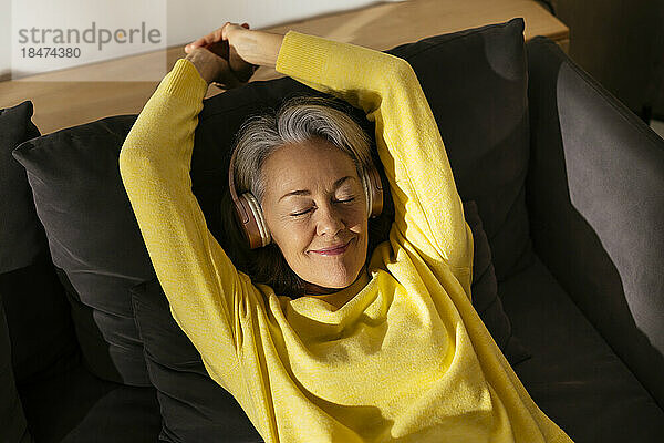 Lächelnde Frau entspannt sich zu Hause auf dem Sofa