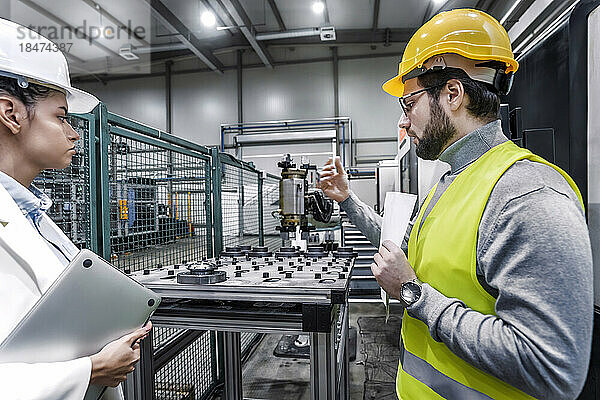 Ingenieur und Kollege mit Schutzhelm diskutieren in der Fabrik