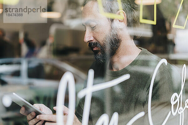 Reifer Mann benutzt Tablet-PC im Café  gesehen durch Glas