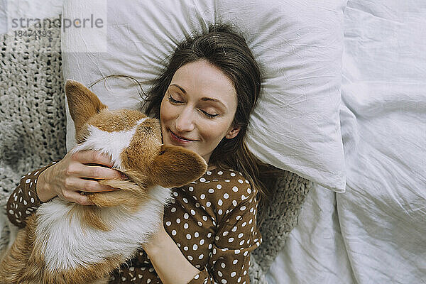 Reife Frau mit geschlossenen Augen liegt mit Hund zu Hause im Bett
