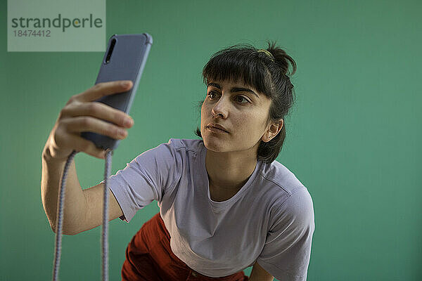 Junge Frau macht Selfie mit Smartphone vor grünem Hintergrund