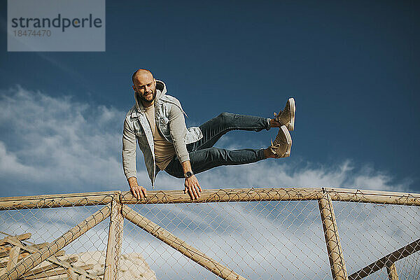 Man jumping over fence under sky