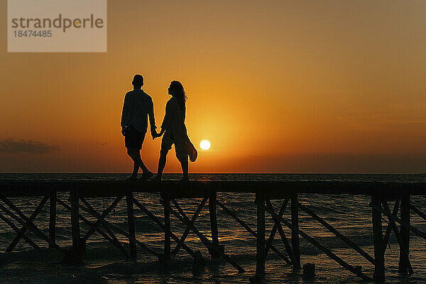 Silhouette eines Paares  das bei Sonnenaufgang auf dem Pier spaziert