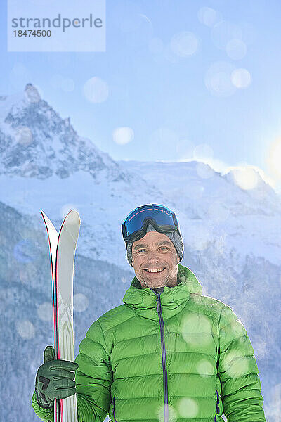 Glücklicher Mann  der an einem sonnigen Tag mit Skiern vor den Bergen steht
