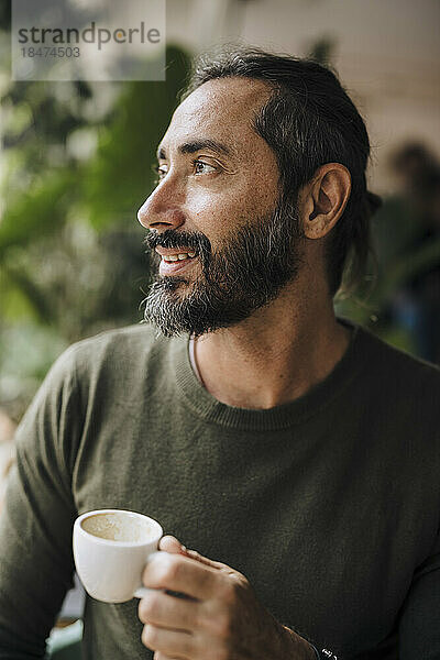 Nachdenklich lächelnder Mann mit Kaffeetasse sitzt im Café