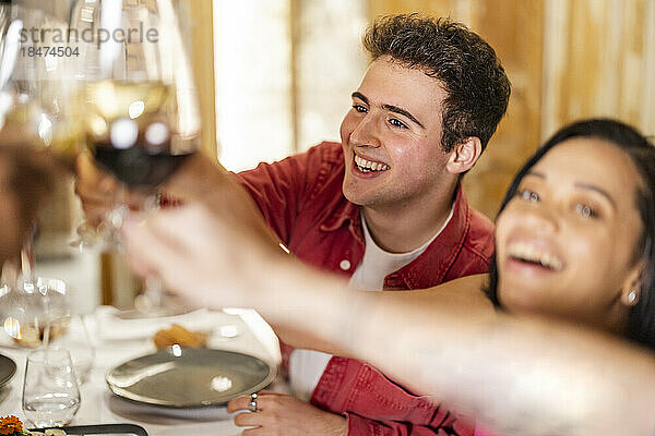 Glücklicher junger Mann  der mit Freunden im Restaurant Weingläser anstößt