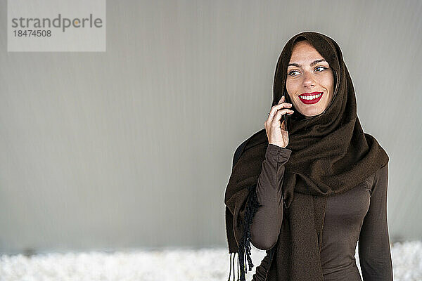 Frau trägt Hijab und spricht mit Smartphone vor der Wand