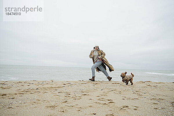 Frau läuft mit Hund im Sand am Strand