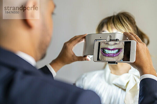 Geschäftsmann fotografiert mit Vergrößerungsgerät das Lächeln eines Kollegen per Mobiltelefon