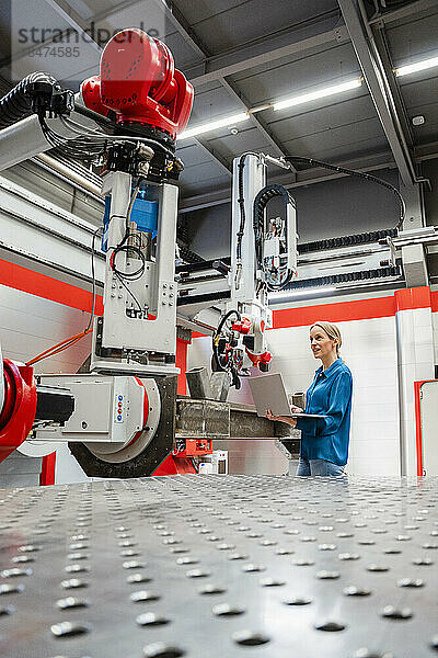 Reifer Ingenieur untersucht Roboter mit Laptop in der Fabrik