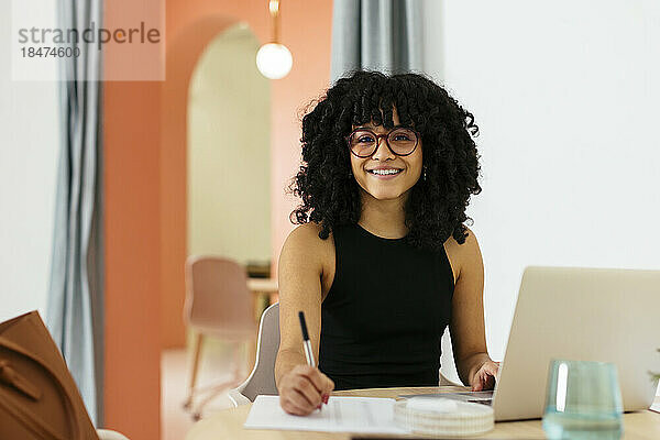 Lächelnde junge Geschäftsfrau mit Afro-Frisur  die am Schreibtisch im Büro arbeitet