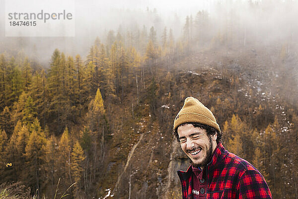 Happy young man standing on mountain in foggy weather