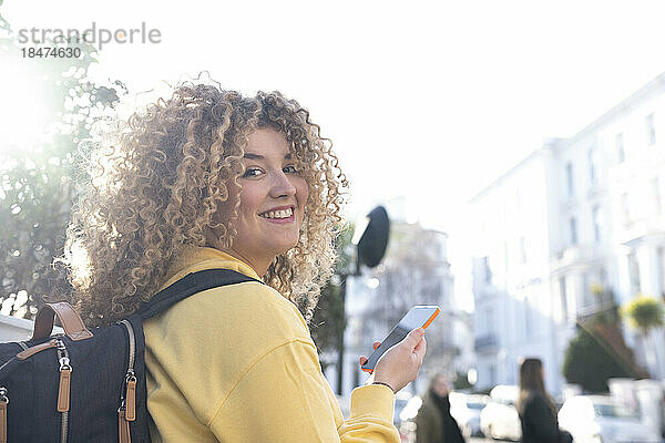 Lächelnde Frau mit Rucksack und Smartphone an einem sonnigen Tag