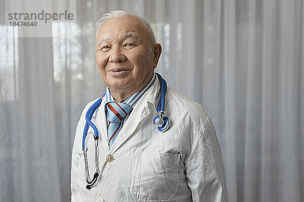 Happy doctor standing in front of window at clinic
