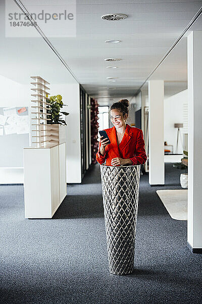 Glückliche Geschäftsfrau mit Smartphone im Pflanzgefäß