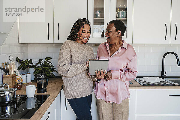 Frau teilt Tablet-PC mit Mutter in der heimischen Küche