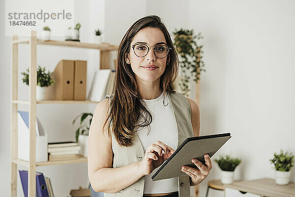 Lächelnde Geschäftsfrau steht mit Tablet-PC im Büro