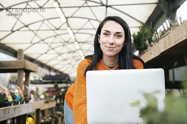 Lächelnde Frau mit Laptop im Gewächshaus