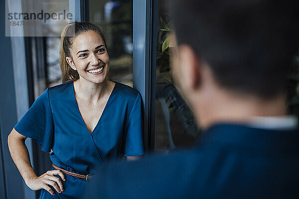 Lächelnde junge Geschäftsfrau im Gespräch mit einem Kollegen im Büro