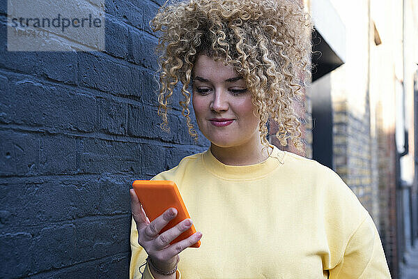 Junge Frau benutzt Mobiltelefon an einer Ziegelwand