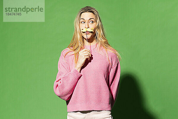Frau imitiert Schnurrbart vor grünem Hintergrund