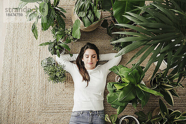 Woman with hands behind head amidst potted plants at home