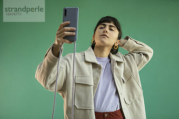 Junge Frau macht ein Selfie mit dem Mobiltelefon vor grünem Hintergrund