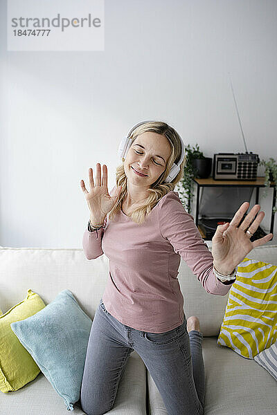 Smiling mature woman wearing wireless headphones dancing at home