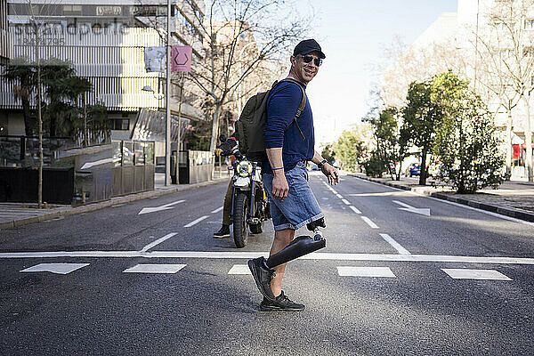 Lächelnder reifer Mann mit amputiertem Bein überquert Straße in der Stadt
