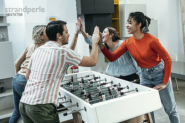 Fröhliche Kollegen  die im Büro Tischfußball spielen und High-Five geben