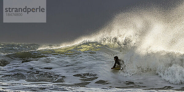 Junger Mann schwimmt im Urlaub mit Surfbrett im welligen Meer